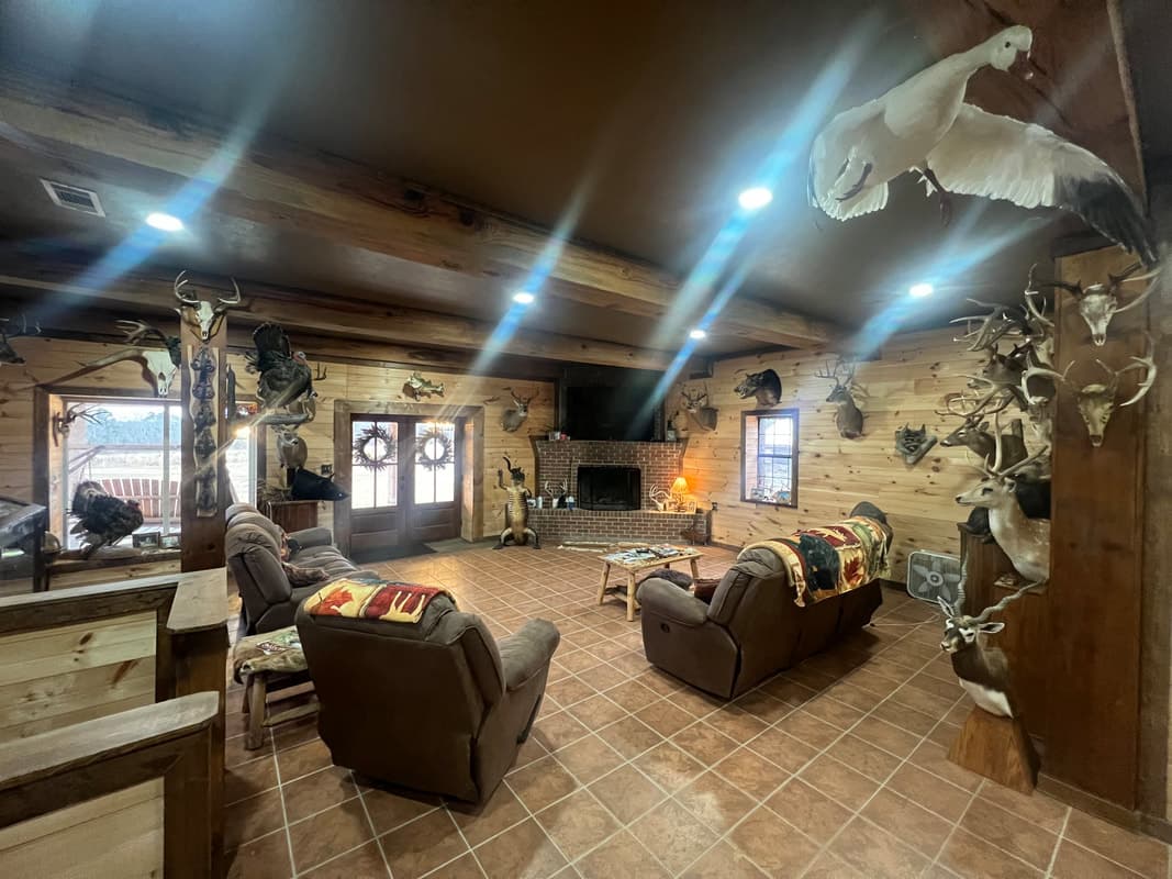 Cozy rustic lodge living room with many mounted deer trophies on wood-paneled walls, a brick fireplace, and comfortable recliners